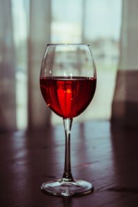 A glass of red wine on a wooden table in front of a window.