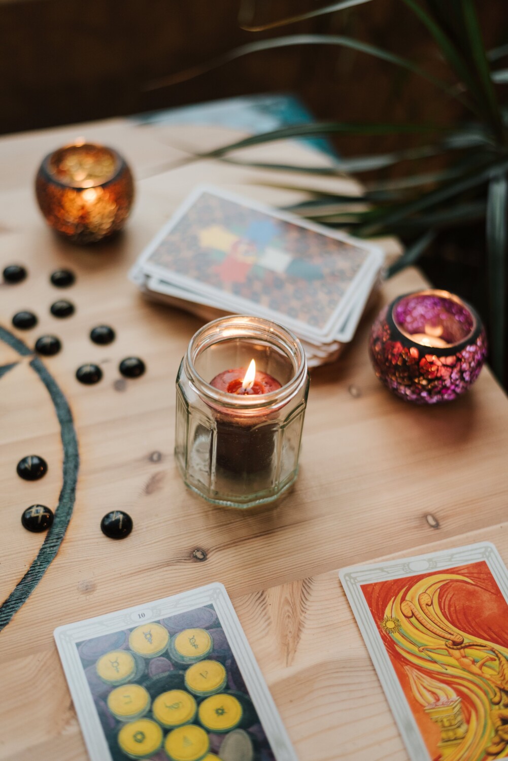 a candle in a glass jar on a wooden table surrounded by other candles and some print artwork